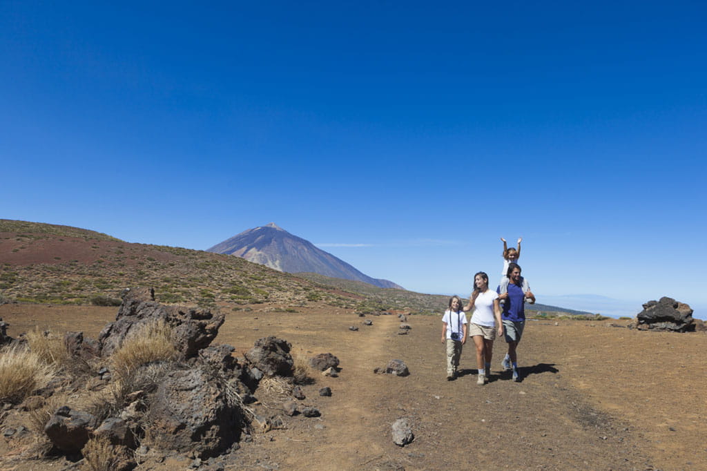 Family walking along a trail on Mount Teide, Tenerife, with the volcano in the background.