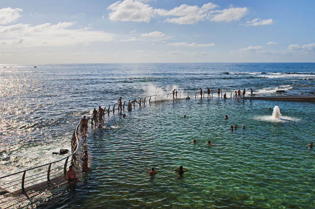 People swim in a natural pool by the sea in Tenerife.