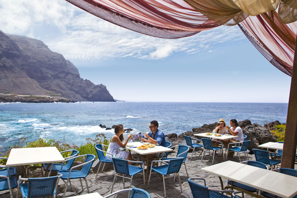 Beachfront terrace in Tenerife with people eating under a clear sky.