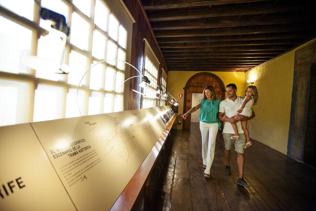Family touring a museum in Tenerife, observing illuminated exhibition in a wooden corridor.