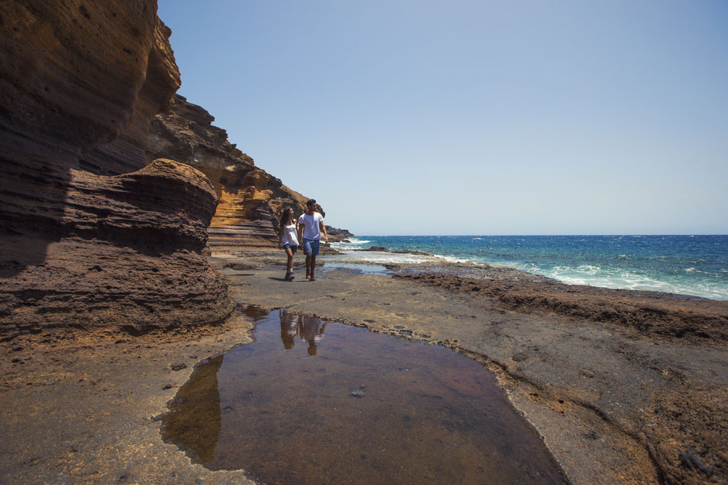 People walking on the rocky coast of Tenerife by the sea.