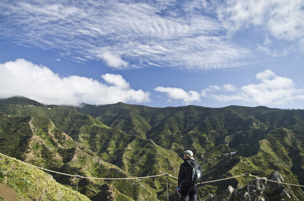 Person watching the green mountains of Anaga in Tenerife under a partly cloudy sky.