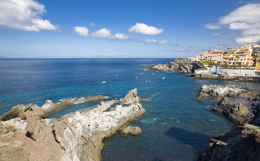 Rocky coastline and buildings in Los Gigantes, Tenerife, with the sea and blue sky.