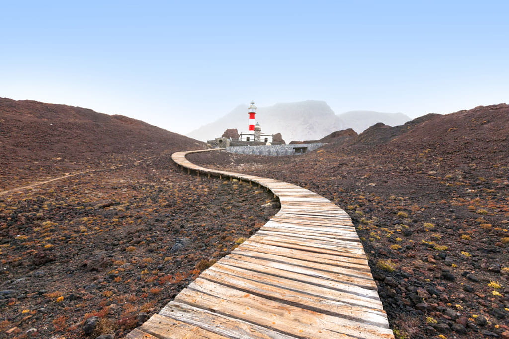 Wooden walkway to the lighthouse of Punta de Teno, Tenerife, with mountains in the background.