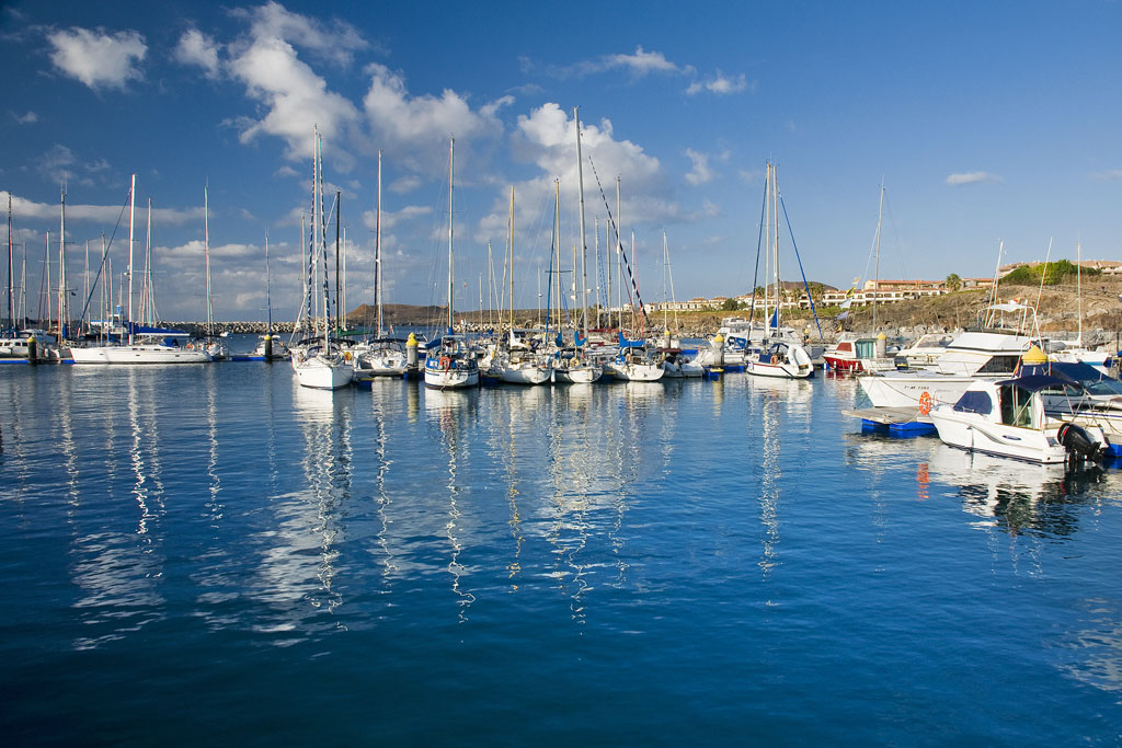 Boats anchored in the port of Las Galletas, Tenerife, under a blue sky.