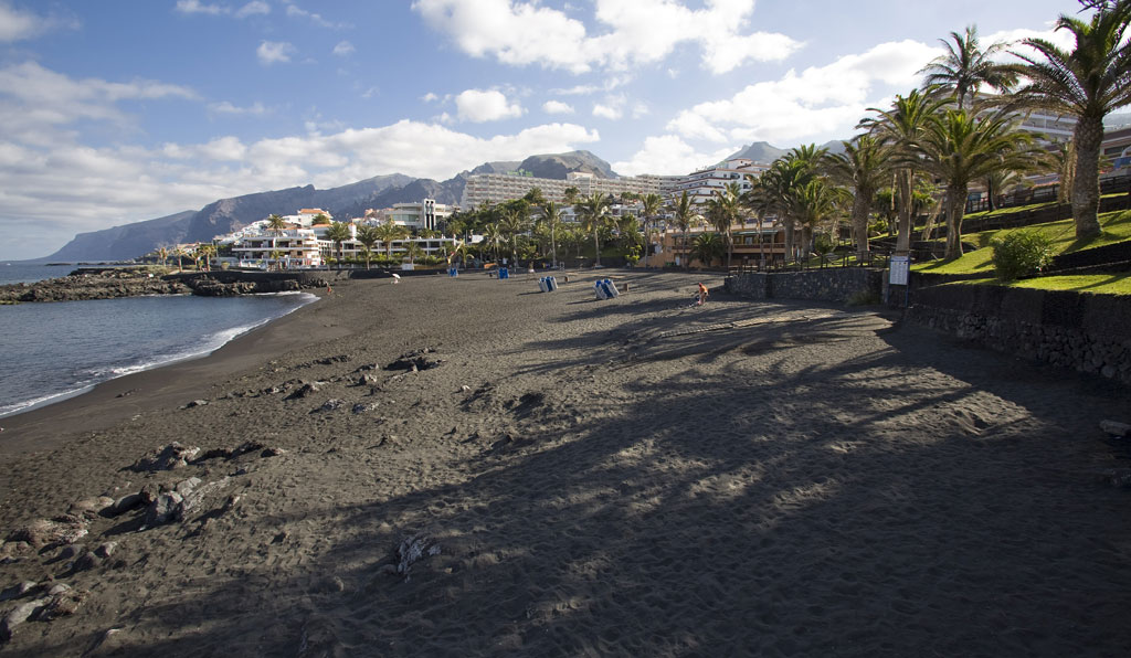 Black sand beach in Los Gigantes, Tenerife, with mountains and buildings in the background.