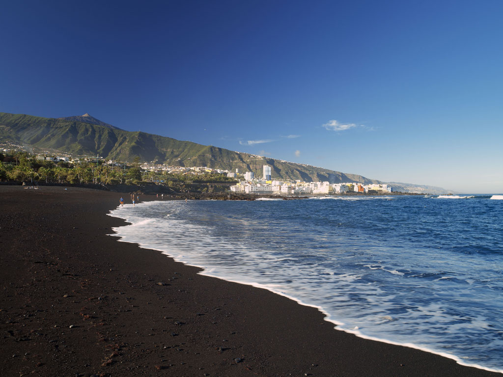 Black sand beach with views of Mount Teide in Tenerife and the city in the background.