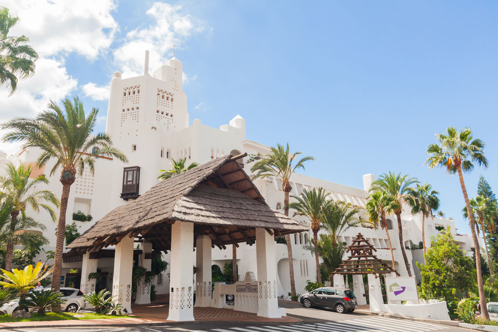 Main entrance of a hotel with white architecture and palm trees in Tenerife.