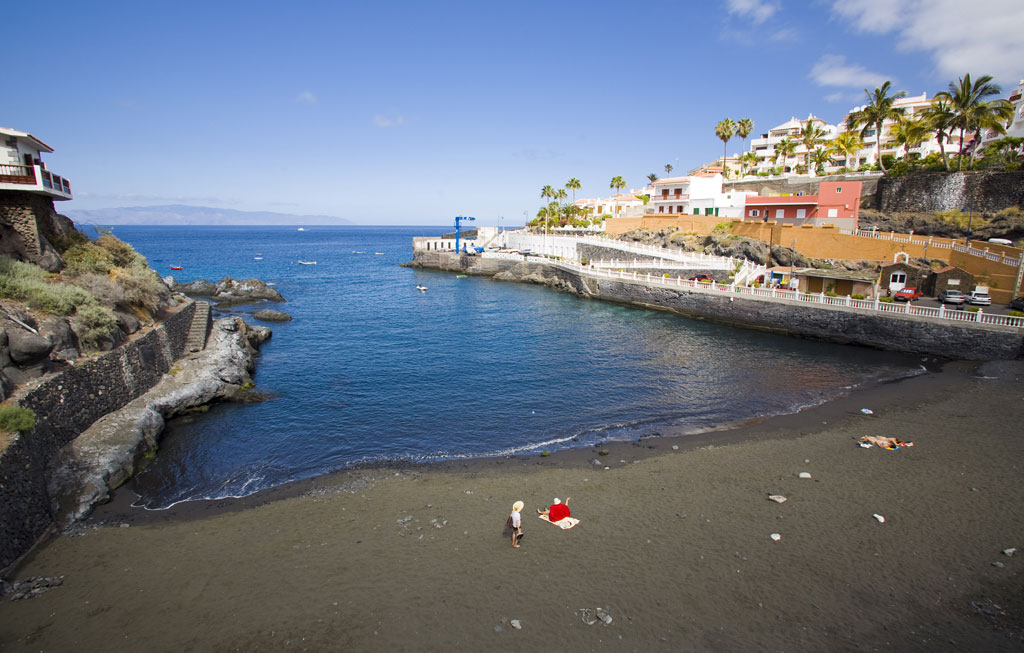 Quiet beach in Alcalá, Tenerife, with houses and palm trees in the background.