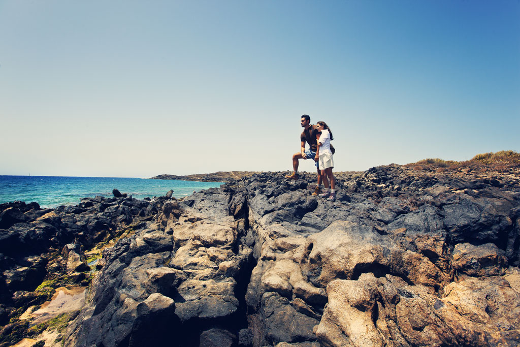 Couple watches the sea from rocky coast in Tenerife.