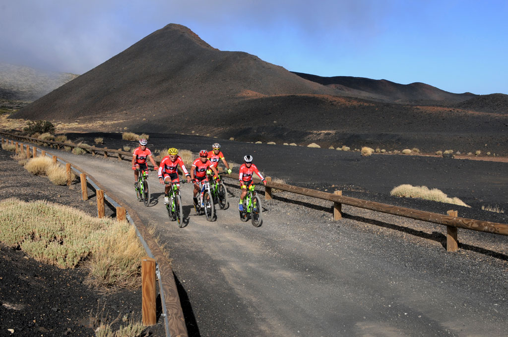 Cyclists on a dirt road, volcanic landscape in Tenerife in the background.