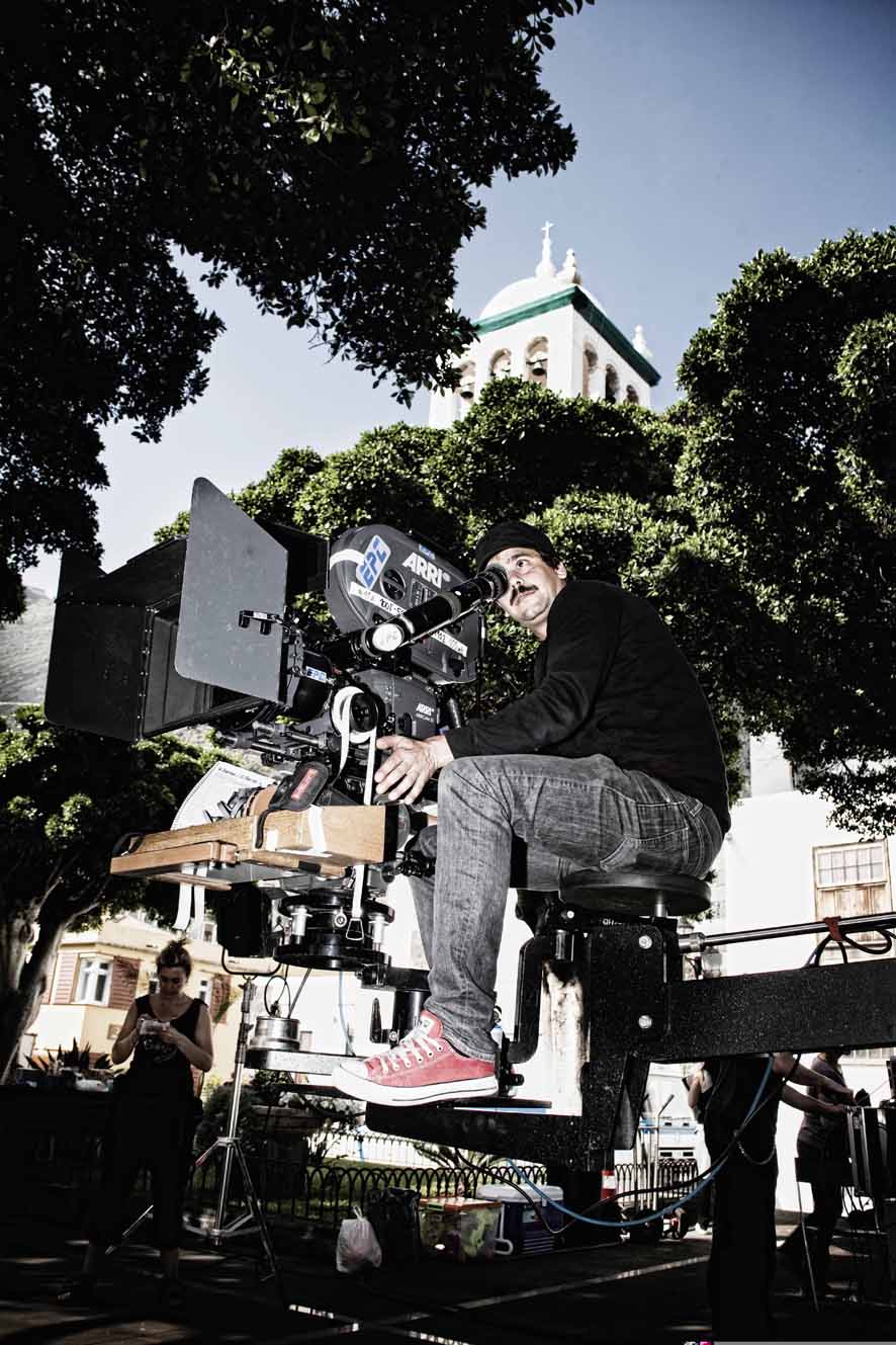 Cameraman operating a camera in a square in Tenerife, with a church tower in the background.