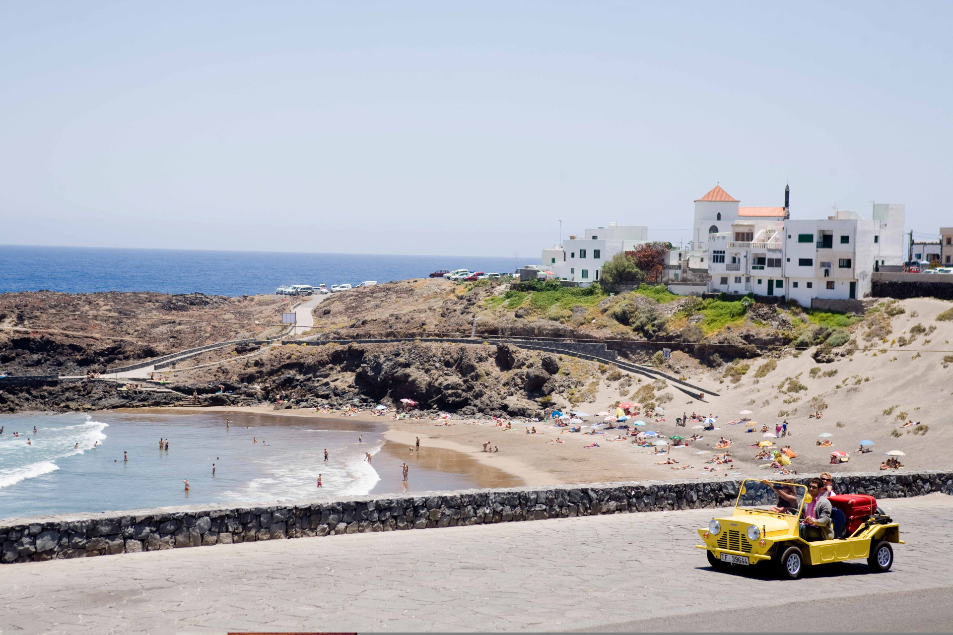 Natural pool beach with tourists and yellow car in La Punta, Tenerife.