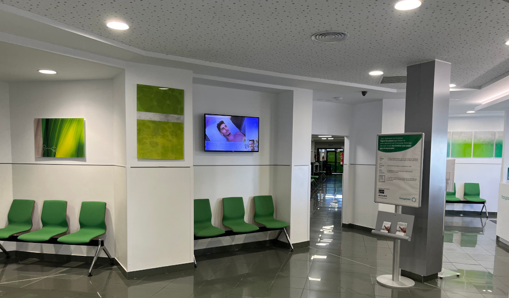 Waiting room with green chairs and lit screens in a clinic in Tenerife.