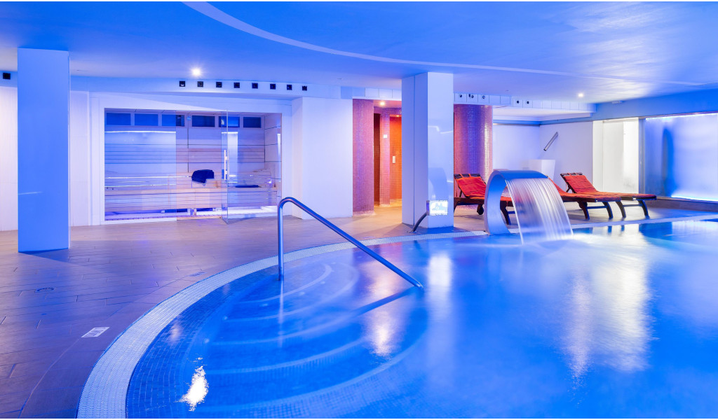 Indoor pool with waterfall and sun loungers in Tenerife spa.