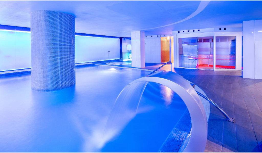 Illuminated indoor swimming pool in a hotel in Tenerife with water jet and modern decoration.
