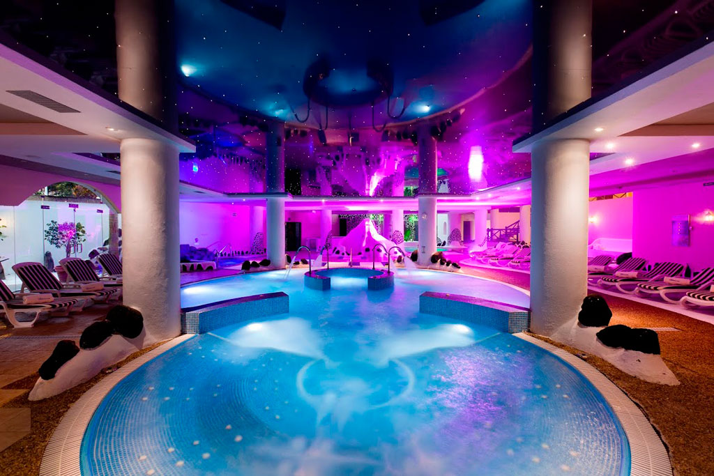 Illuminated indoor pool in Tenerife spa with sun loungers all around.