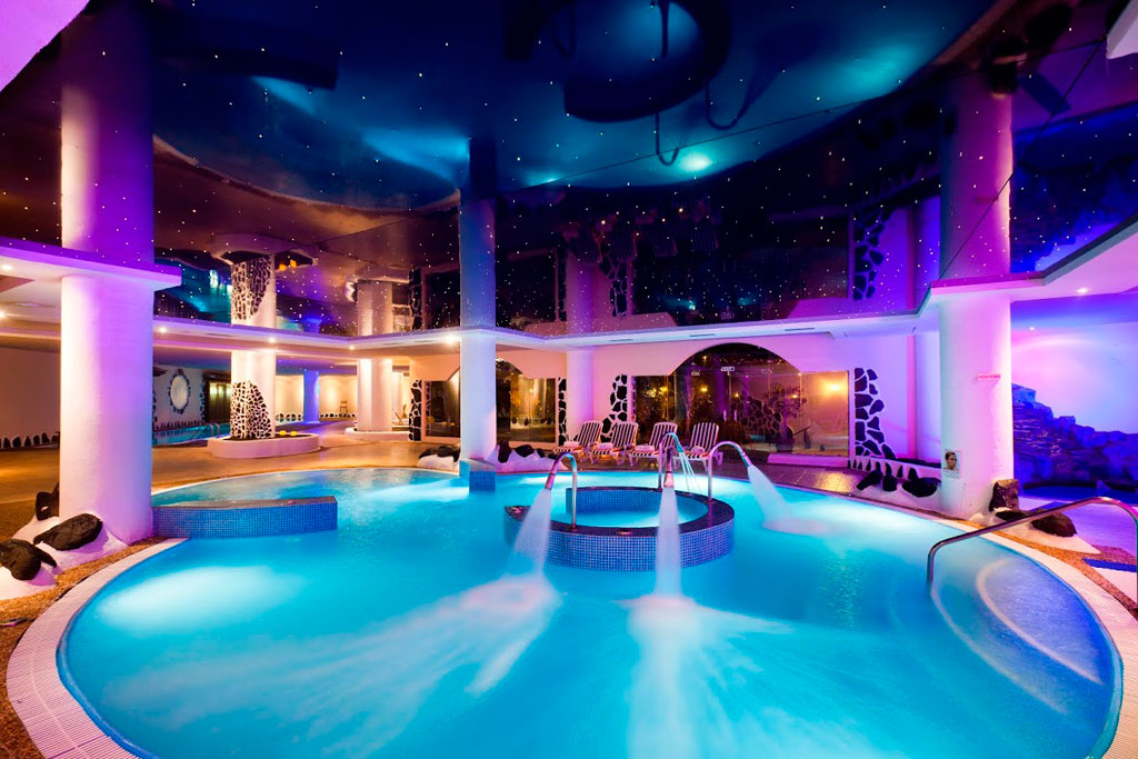 Illuminated indoor swimming pool in hotel in Tenerife with columns and starry ceiling.