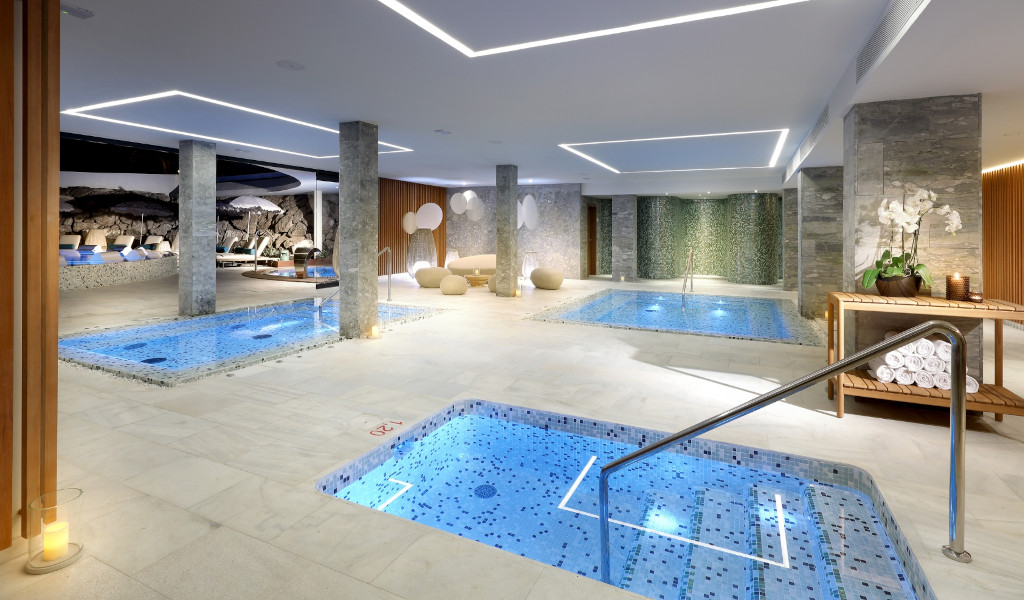 Indoor swimming pool with jacuzzi in a spa in Tenerife, surrounded by plants and lamps.