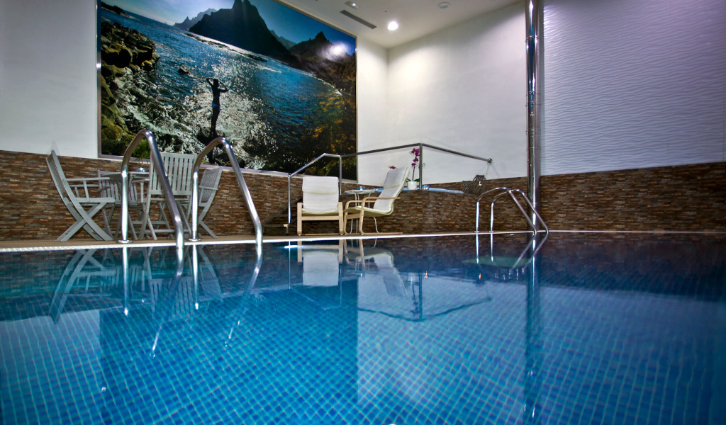Indoor pool with chairs and a photo of a Tenerife landscape on the wall.