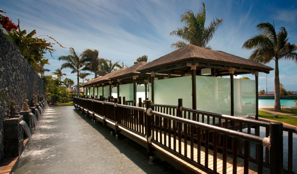 Wooden walkway with palm trees and walls at Hotel Villa Cortés Tenerife.