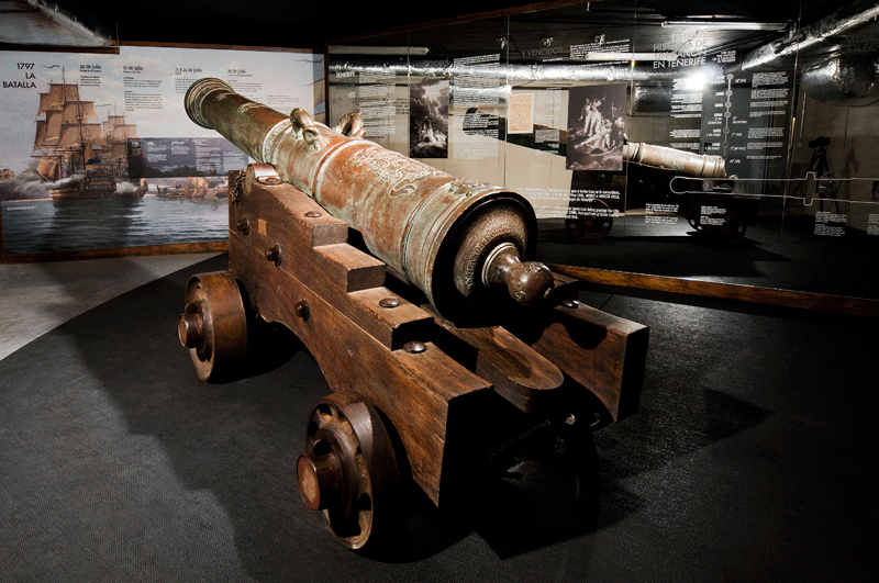 Ancient cannon on display in a museum in Tenerife, with information panels behind it.