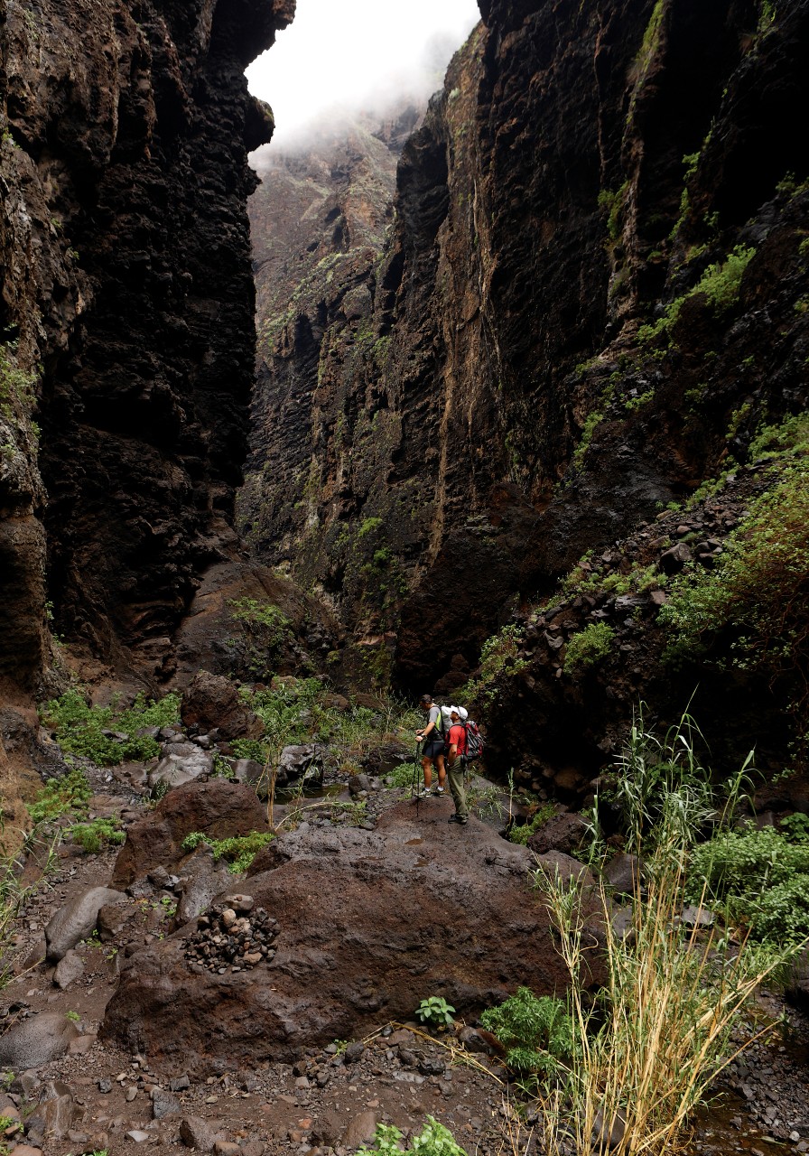 Two people walking through the Barranco de Masca in Tenerife surrounded by high rock walls.