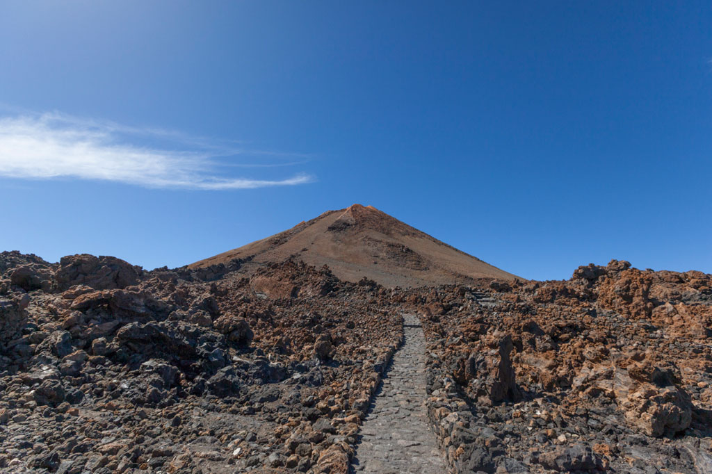 A pebble path to Mount Teide in Tenerife under a blue sky.