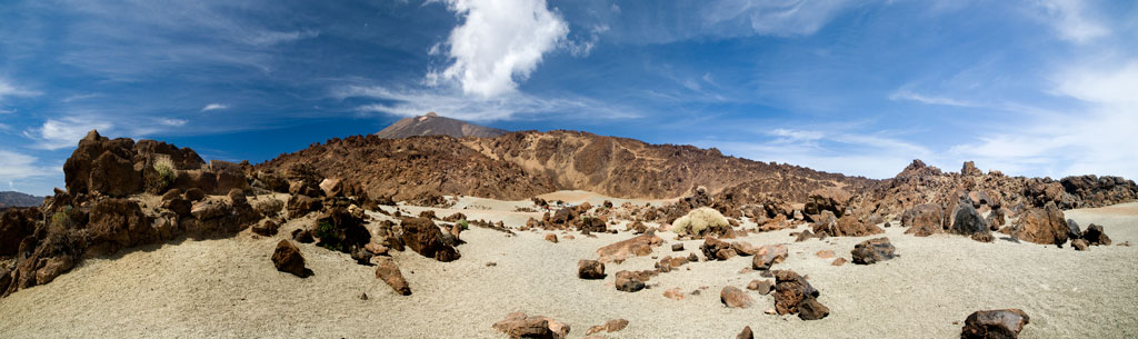 Volcanic landscape of Mount Teide in Tenerife under a blue sky with scattered clouds.