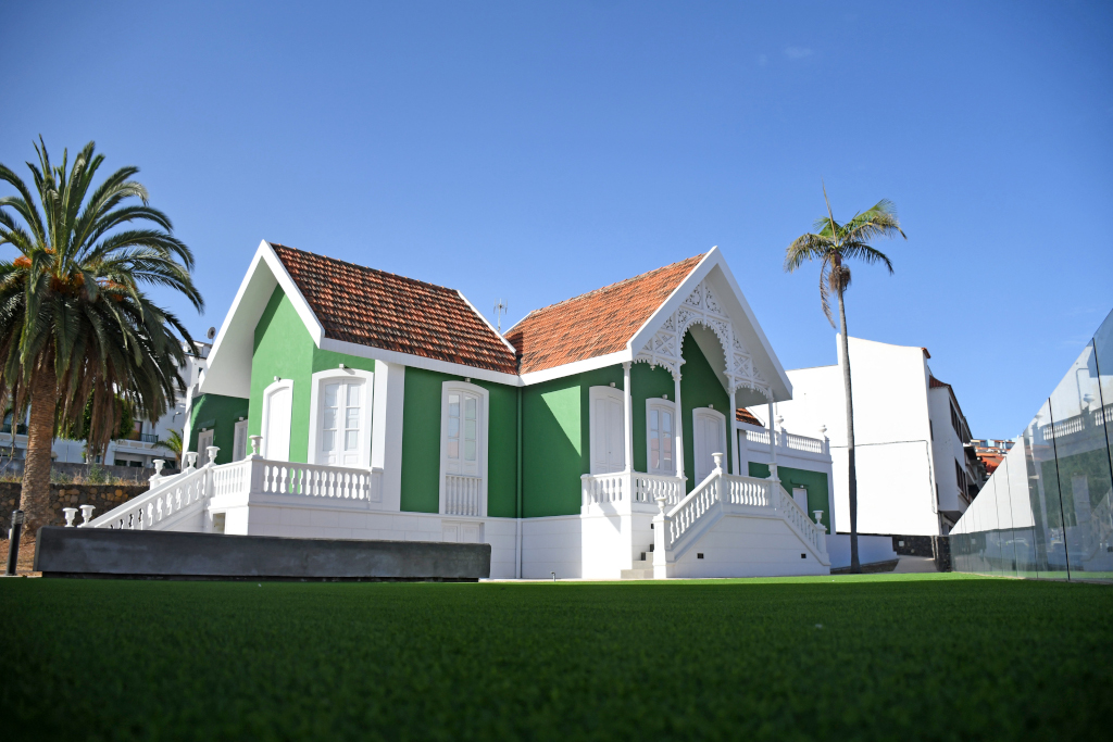 Old green and white house with red roof in Tenerife, surrounded by palm trees and lawns.