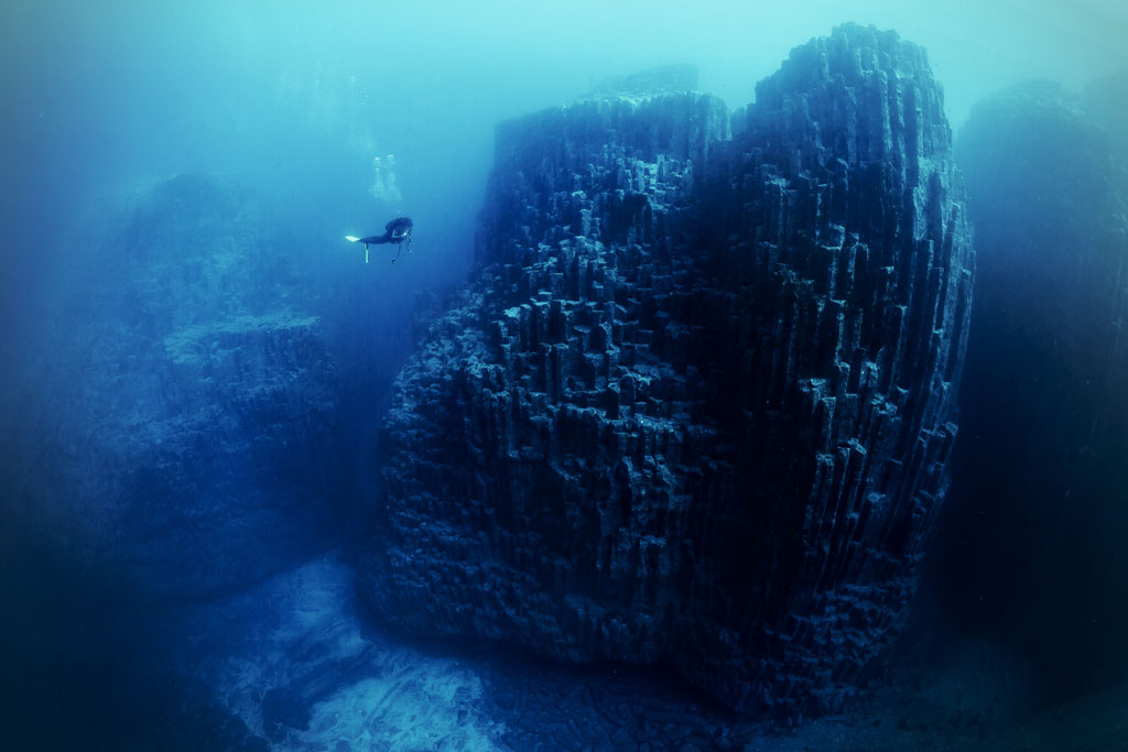 Diver swimming near underwater basalt columns in Tenerife.