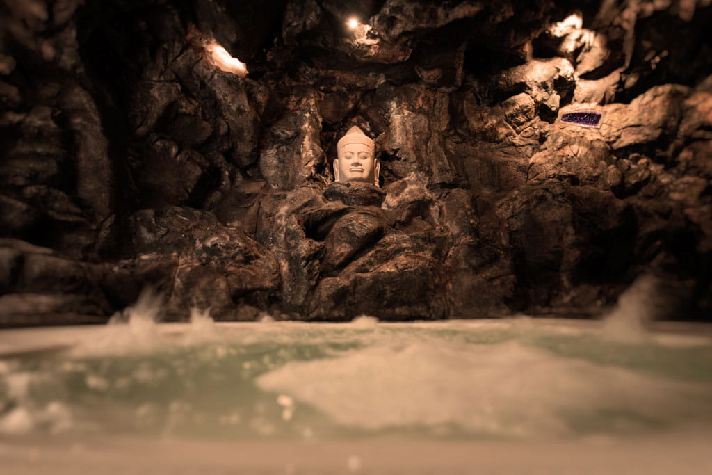 Bust of Buddha in rocky cave with water at the base in Tenerife.