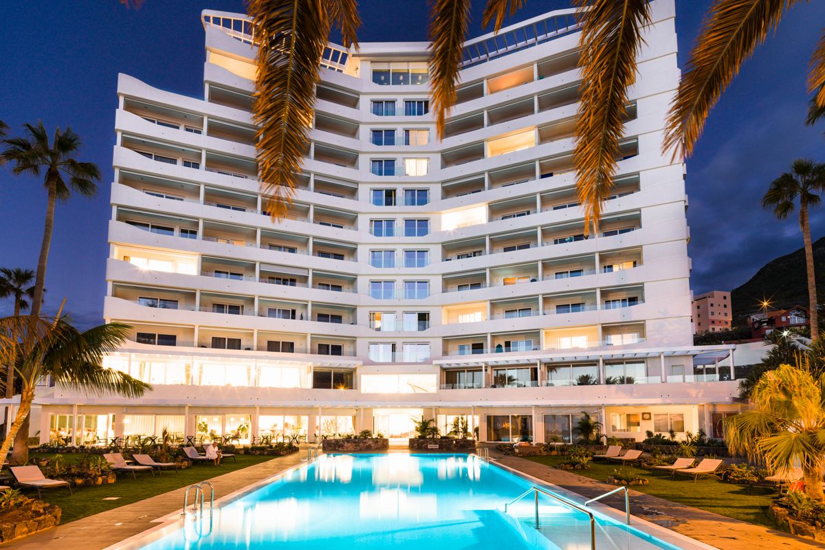 Building with swimming pool illuminated at dusk in Tenerife, surrounded by palm trees.