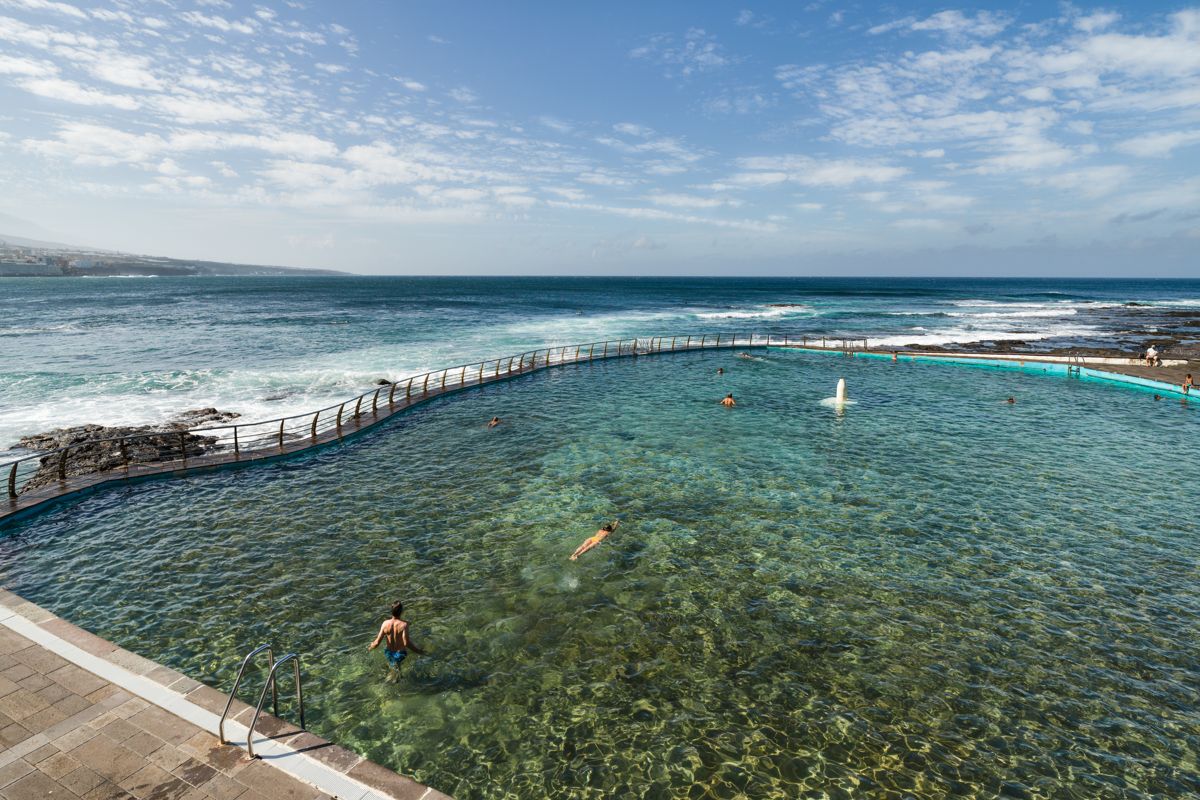 Natural pool in Tenerife by the ocean with several people swimming.