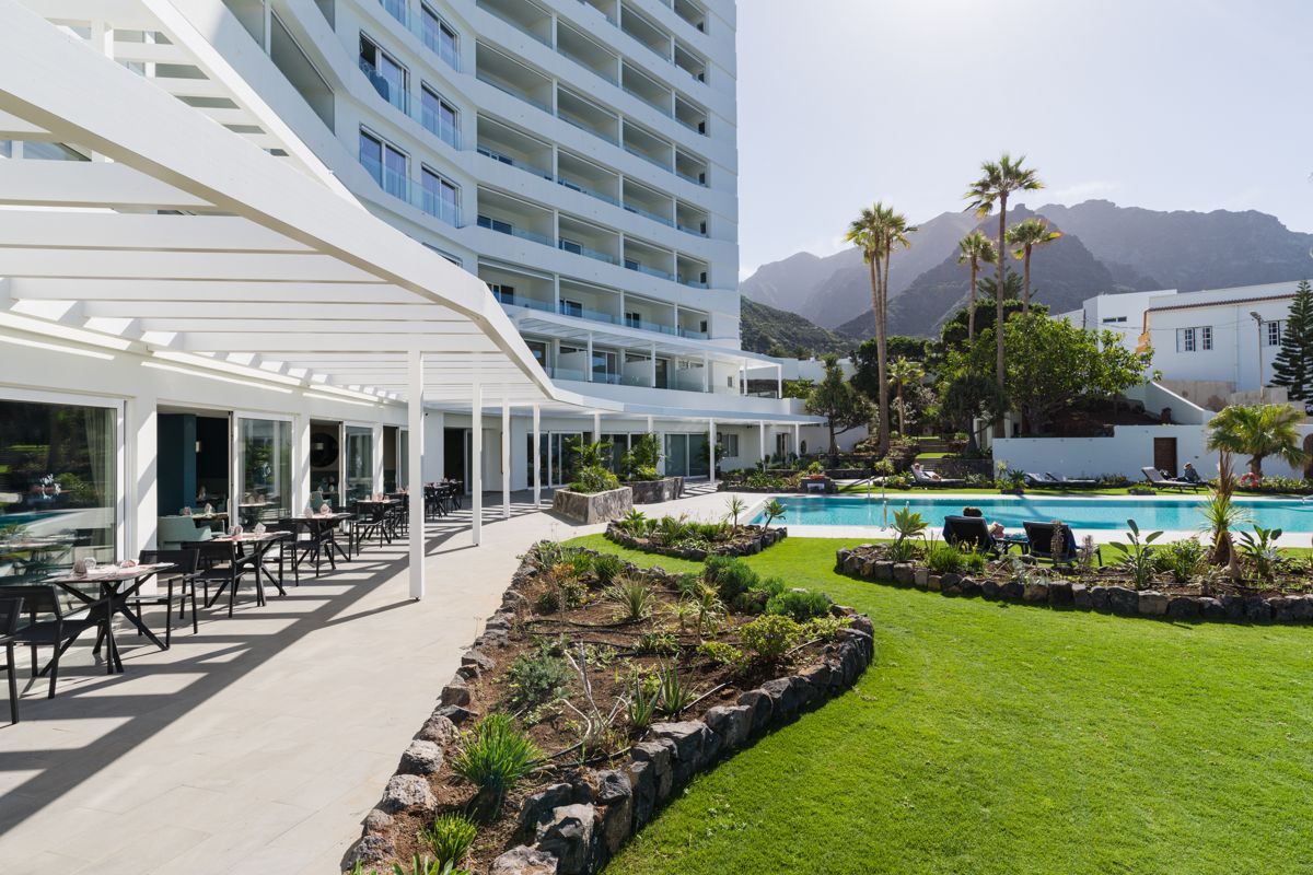 Terrace of a hotel in Tenerife with tables, swimming pool and mountains in the background.